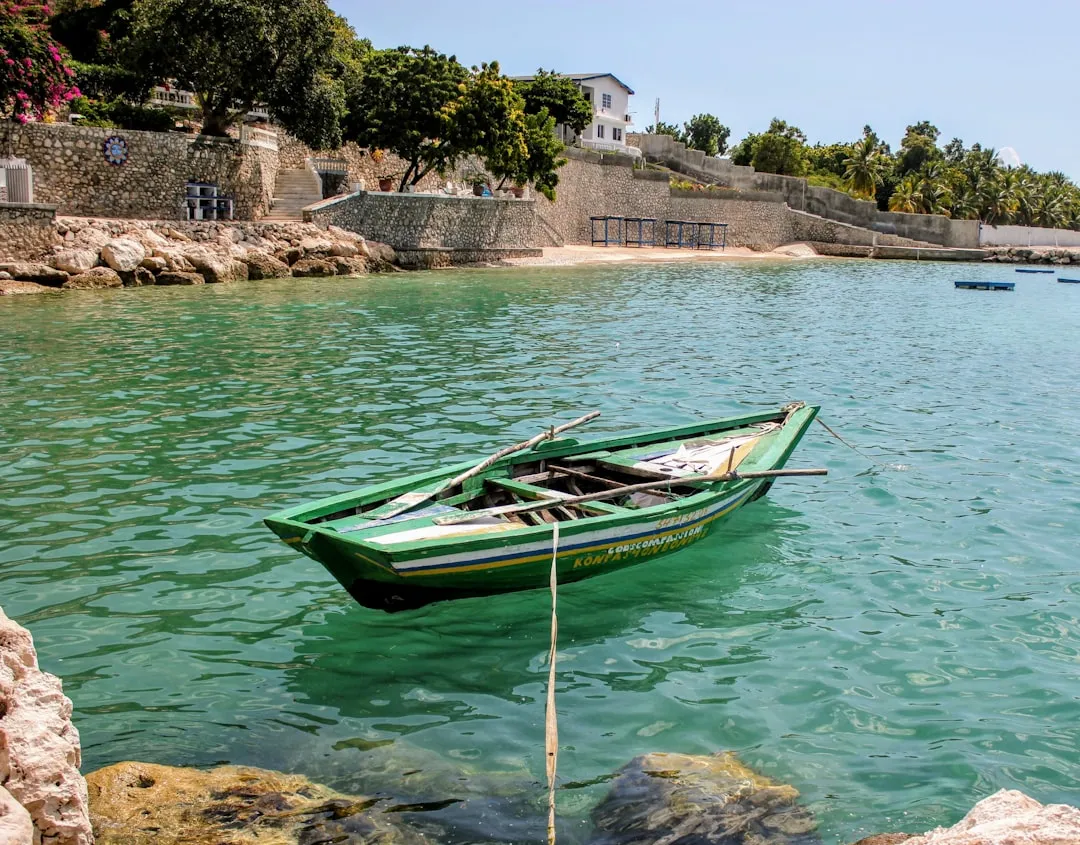 Una barca de pesca verde fondeada en agua turquesa, junto a un pueblo costero.